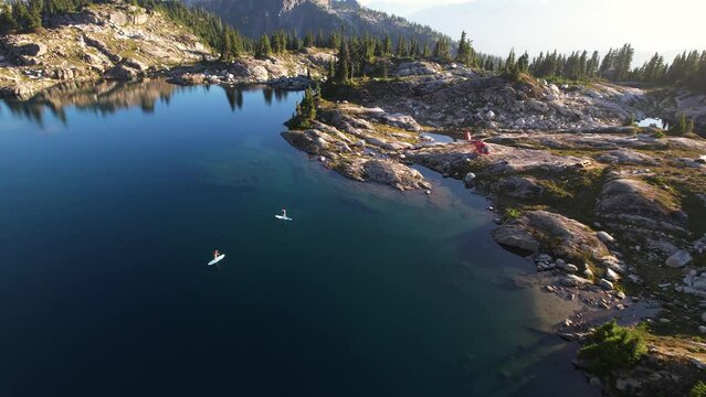 Couple paddleboarding on an alpine lake in the mountains with rocky shore