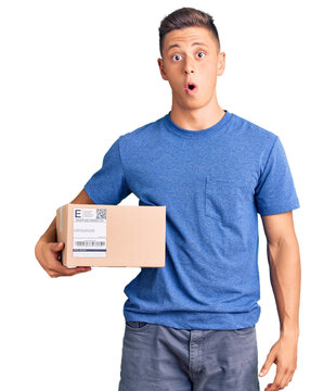 Young handsome hispanic man holding delivery package scared and amazed with open mouth for surprise, disbelief face