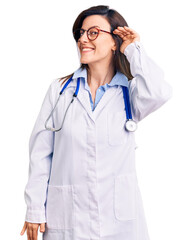 Young beautiful woman wearing doctor stethoscope and glasses smiling with hand over ear listening an hearing to rumor or gossip. deafness concept.