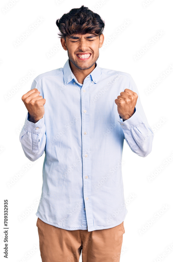 Poster Young hispanic man wearing casual shirt very happy and excited doing winner gesture with arms raised, smiling and screaming for success. celebration concept.