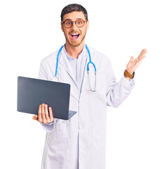 Handsome young man with bear wearing doctor uniform working using computer laptop celebrating victory with happy smile and winner expression with raised hands