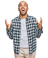 Naklejka premium Hispanic adult man wearing casual clothes crazy and mad shouting and yelling with aggressive expression and arms raised. frustration concept.