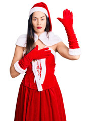 Young beautiful caucasian woman wearing santa claus costume swearing with hand on chest and open...