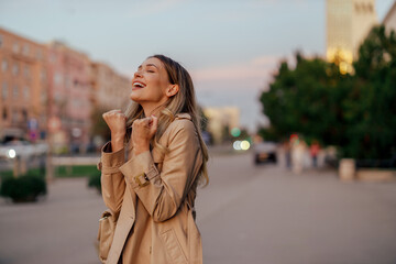 Fototapeta premium A young trendy woman is celebrating winning and prize on a street.