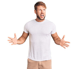 Young caucasian man wearing casual white tshirt crazy and mad shouting and yelling with aggressive expression and arms raised. frustration concept.
