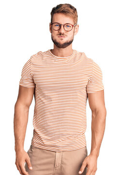 Young caucasian man wearing casual clothes and glasses puffing cheeks with funny face. mouth inflated with air, crazy expression.