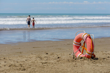 Lifebuoy on a beach and people out of focus in the background.