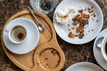 An after-meal scene with an empty coffee cup, a crumpled napkin, and croissant crumbs on a wooden tray and a white plate.