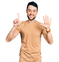 Hispanic man with beard wearing casual t shirt showing and pointing up with fingers number seven while smiling confident and happy.