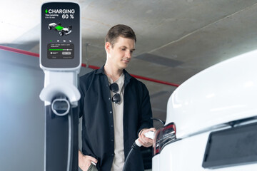 Young man travel with EV electric car to shopping center parking lot charging in downtown city...
