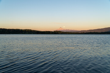 landscape image tranquil movement of a lake, with a towering volcano in the background and a full moon rising during the enchanting sunset.