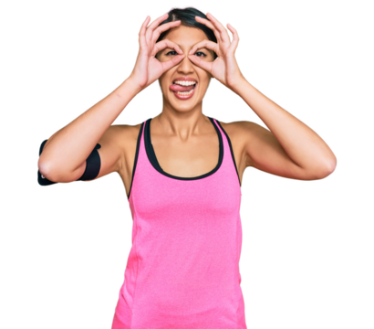 Beautiful asian young sport woman wearing sportswear and arm band doing ok gesture like binoculars sticking tongue out, eyes looking through fingers. crazy expression.