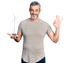 Middle age hispanic with grey hair holding solar windmill for renewable electricity doing ok sign with fingers, smiling friendly gesturing excellent symbol