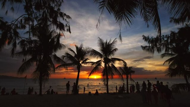 Silhouetted people and palms near sea. Sunset at tropical White beach, Boracay island, Philippines, slow motion 4k