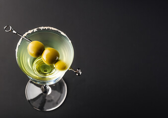 closeup photo of fresh cold  martini cocktail glass with gin and olive isolated on black background. top angle