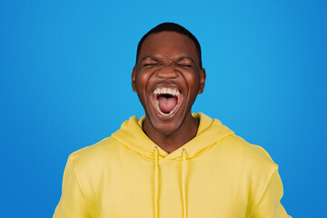 An exultant African man in a yellow hoodie laughs heartily with his mouth wide open