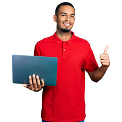 Young african american man working using computer laptop smiling happy and positive, thumb up doing excellent and approval sign