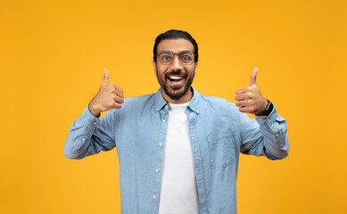 Enthusiastic man in a blue denim shirt giving two thumbs up, wide-eyed and smiling