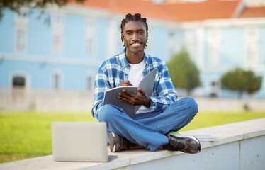 Fototapeta na wymiar Happy african american student guy with laptop sitting outdoor