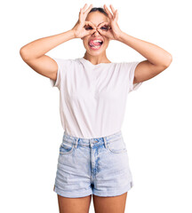 Young beautiful blonde woman wearing casual white tshirt doing ok gesture like binoculars sticking tongue out, eyes looking through fingers. crazy expression.