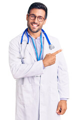 Fototapeta premium Young hispanic man wearing doctor uniform and stethoscope cheerful with a smile on face pointing with hand and finger up to the side with happy and natural expression