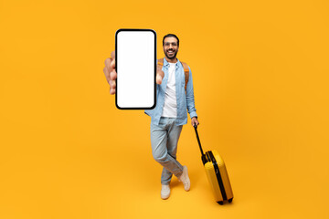 Happy indian man traveler in casual with yellow suitcase, enjoy adventure, show phone with empty...