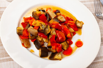 Delicious homemade saute of eggplant, bell pepper, carrots, tomato and pieces of pork bacon garnished with greens
