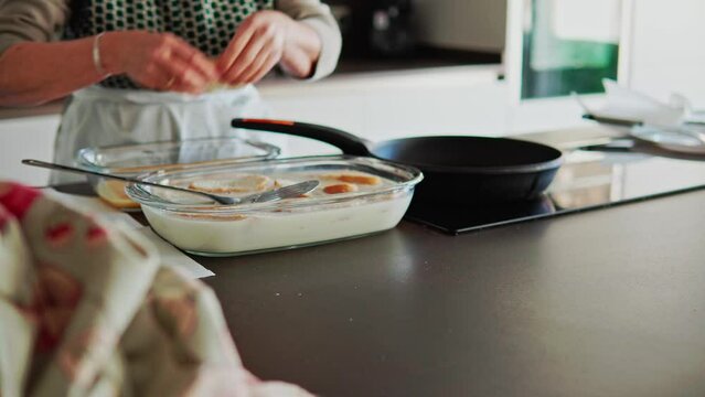 Senior woman on the kitchen soaking bread in milk and egg to make traditional torrijas for her family on Easter festivities