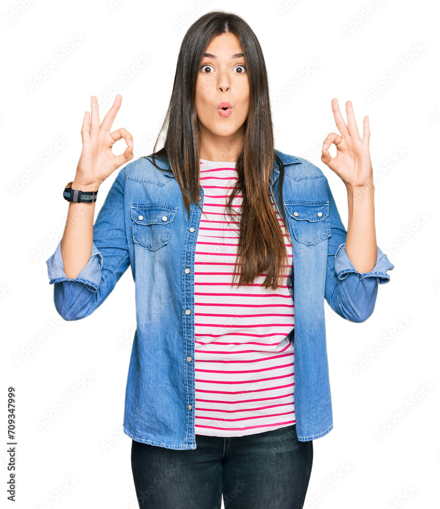 Poster Young brunette woman wearing casual clothes looking surprised and shocked doing ok approval symbol with fingers. crazy expression