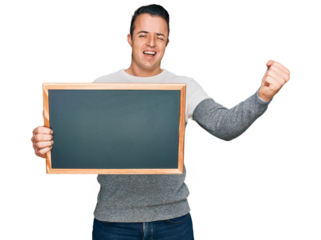 Handsome young man holding blackboard screaming proud, celebrating victory and success very excited with raised arms