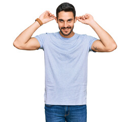 Young hispanic man wearing casual clothes smiling pulling ears with fingers, funny gesture....