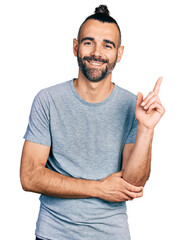 Hispanic man with ponytail wearing casual grey t shirt with a big smile on face, pointing with hand...