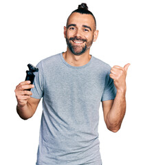 Hispanic man with ponytail holding electric razor machine pointing thumb up to the side smiling...