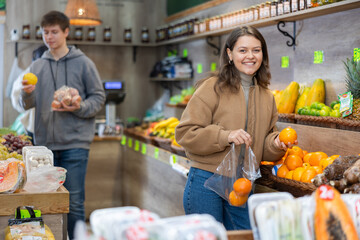 Young woman selects and buys fresh oranges in a grocery store