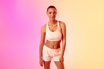 A confident young lady athlete with a short haircut poses in a sports bra and running shorts