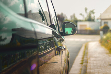 rückspiegel eines pkw auf einem parkplatz neben einem haus bei strahlender sonne mit stahlen - obrazy, fototapety, plakaty