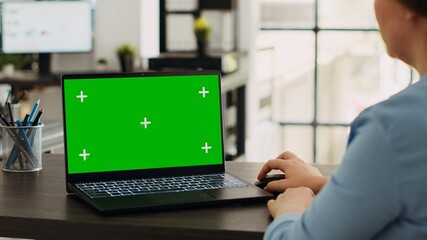 Company specialist using laptop with greenscreen template, working with mockup chromakey display on pc. Woman analyzing isolated copyspace layout on screen, works at office desk.