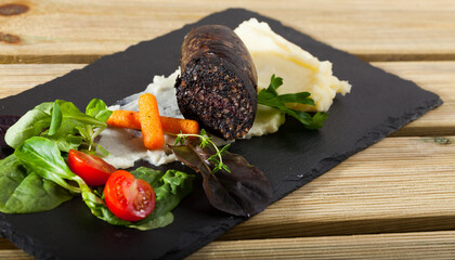 Delicious blood sausage with garnish of mashed potatoes, carrots, tomatoes and greens