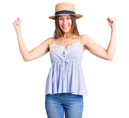 Beautiful brunette young woman wearing summer hat screaming proud, celebrating victory and success very excited with raised arms