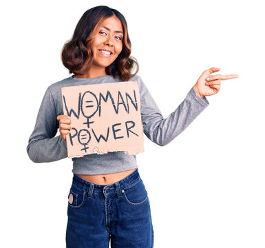 Young beautiful mixed race woman holding woman power banner smiling happy pointing with hand and finger to the side