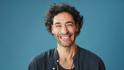 Close up, laughing man looks at camera isolated on blue background in studio