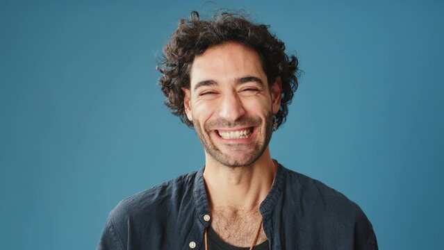 Close up, laughing man looks at camera isolated on blue background in studio
