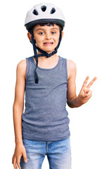 Little cute boy kid wearing bike helmet smiling with happy face winking at the camera doing victory sign. number two.