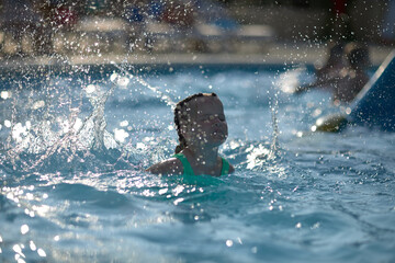 a 4-year-old girl in the pool rides down a slide, splashes of joy and the charm of the child...