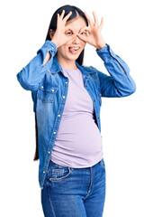 Young beautiful chinese woman pregnant expecting baby doing ok gesture like binoculars sticking tongue out, eyes looking through fingers. crazy expression.