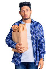 Handsome latin american young man holding paper bag with bread depressed and worry for distress, crying angry and afraid. sad expression.