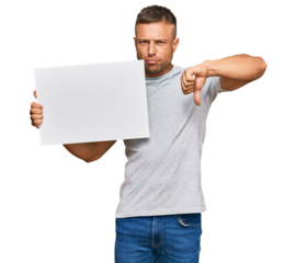 Handsome muscle man holding blank empty banner with angry face, negative sign showing dislike with thumbs down, rejection concept