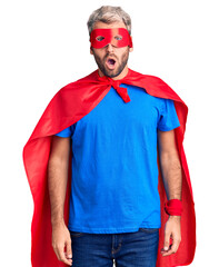 Young blond man wearing super hero custome afraid and shocked with surprise expression, fear and excited face.