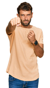 Handsome young man with beard wearing casual tshirt punching fist to fight, aggressive and angry attack, threat and violence
