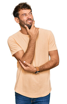 Handsome young man with beard wearing casual tshirt thinking worried about a question, concerned and nervous with hand on chin